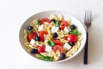 Pasta salad with farfalle, tomatoes, cheese, olives and basil. Italian cuisine. Vegetarian food.