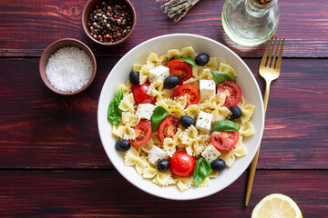 Pasta salad with farfalle, tomatoes, cheese, olives and basil. Italian cuisine. Vegetarian food.