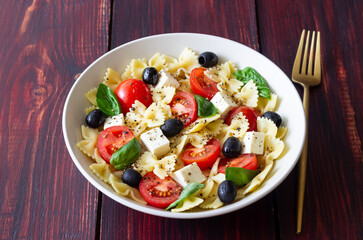 Pasta salad with farfalle, tomatoes, cheese, olives and basil. Italian cuisine. Vegetarian food.