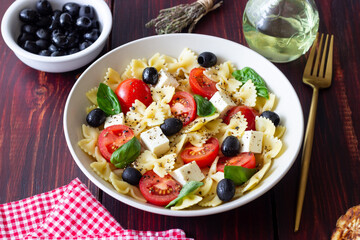 Pasta salad with farfalle, tomatoes, cheese, olives and basil. Italian cuisine. Vegetarian food.
