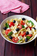 Pasta salad with farfalle, tomatoes, cheese, olives and basil. Italian cuisine. Vegetarian food.