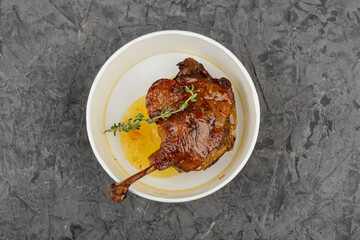 Roasted duck leg with side dish in a disposable plate on a gray background