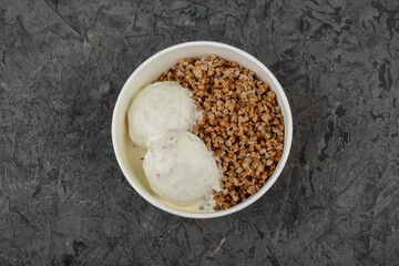 Buckwheat with meatballs in a creamy sauce in a disposable plate on a gray concrete background