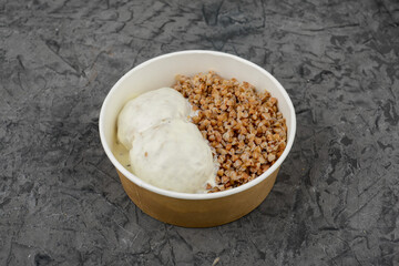 Buckwheat with meatballs in a creamy sauce in a disposable plate on a gray background