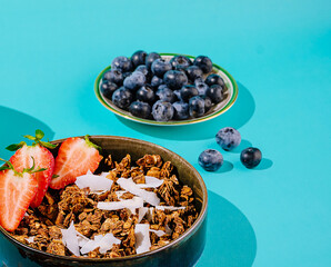 Granola bowl with fresh strawberries and blueberries on turquoise