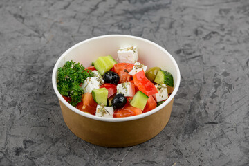 Greek salad in a disposable plate on a gray background