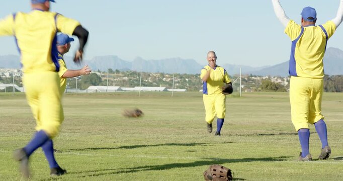 Reacting to fly ball, diverse male teammates catching with glove and celebrating catch on field