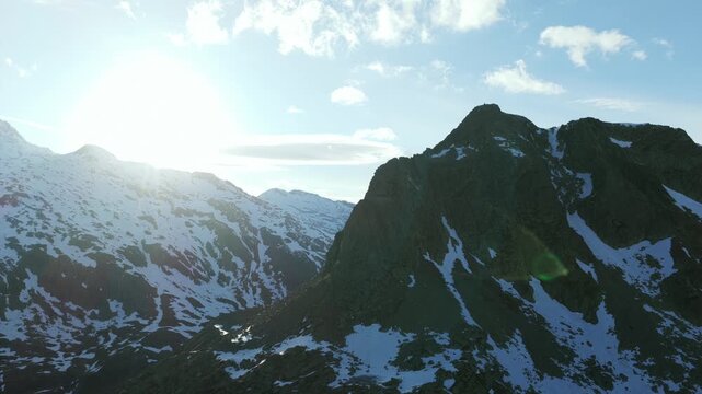 Majestic snow-covered mountains, bright sun creates lens flare over rugged peaks, Italian Alps, Italy. Aerial drone panoramic view