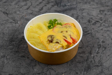Potatoes with omelette with vegetables in a disposable plate on a gray concrete background