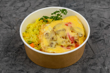 rice with vegetables and omelet with vegetables in a disposable plate on a gray concrete background macro