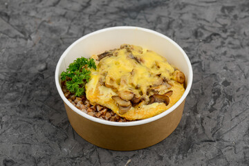 Buckwheat porridge with meat chop and cheese in a disposable plate on a gray background
