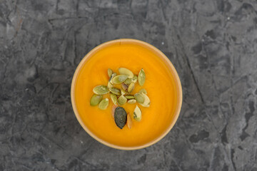 Pumpkin cream soup with seeds in a disposable plate on a gray background