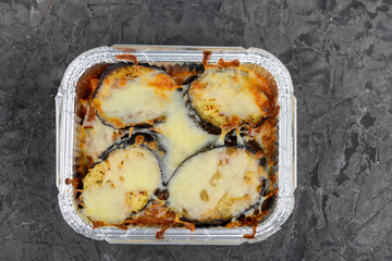 baked eggplant with cheese in a disposable plate on a gray background