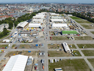 Munich, Germany - 18 August 2025: Aerial view of the Messe MÃ¼nchen exhibition grounds, a vibrant tapestry of white tents and colorful structures against a backdrop of the city's skyline.