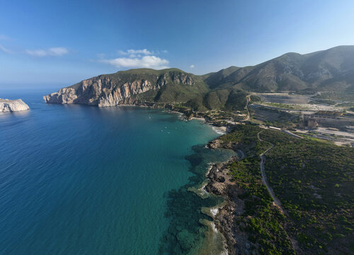 Aerial view of the rugged coastline where turquoise waters meet the rocky shores near the iconic Pan di Zucchero sea stack, Masua, Sardinia, Italy.