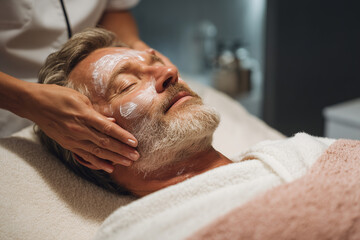 Relaxed mature man receiving a soothing facial treatment with cream in a spa setting for skin care and wellness