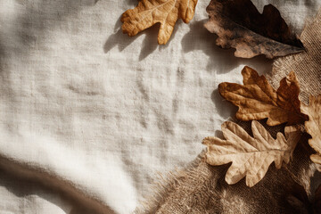 Autumn flat lay with dried oak leaf on beige linen fabric and burlap, warm sunlight creates cozy seasonal atmosphere, perfect for fall backgrounds or rustic designs
