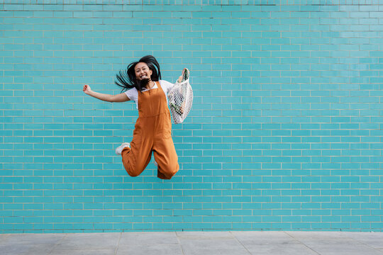 Happy person jumping in front of turquoise wall with reusable shopping bag