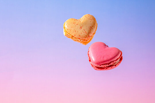 Heart shaped pink and yellow macarons on pastel gradient background