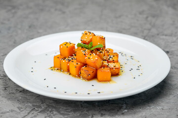 baked pumpkin with sesame seeds in a white plate on a gray background