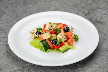 Greek salad with olives in a white plate on a gray concrete background