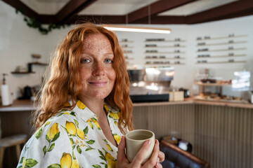 Business owner in lemon shirt holding mug at modern coffee shop
