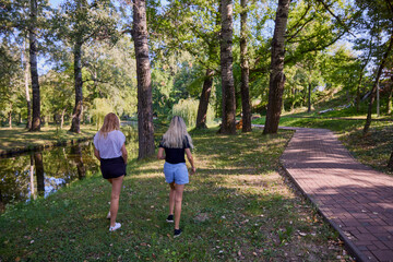 Fototapeta premium Two middle-aged sisters spending a summer morning in the park by a lake relaxing and having fun.