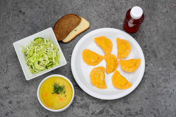 set of fried dumplings, salad and soup in a white plate on a gray background