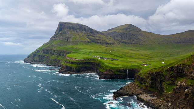 Aerial view of the cascading M&Atilde;&ordm;lafossur Waterfall meeting the turbulent sea below, surrounded by verdant hills and dramatic cliffs, G&Atilde;&iexcl;sadalur, V&Atilde;&iexcl;gar, Faroe Islands.