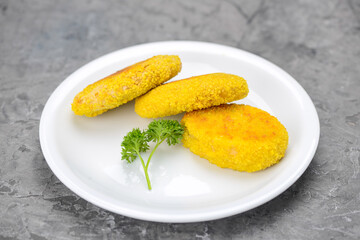 Chicken cutlet in batter in a white plate with greens on a gray concrete background