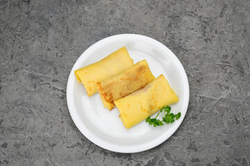 three pancakes with filling in a white plate on a gray concrete background