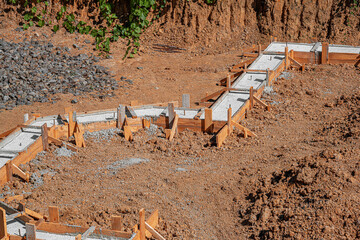 A building foundation with wooden formwork filled with fresh concrete is shown on a construction...