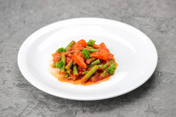 stewed asparagus beans with tomatoes in a white plate on a gray background