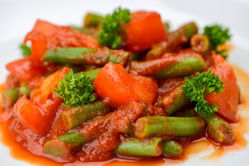 stewed asparagus beans with tomatoes in a white plate macro