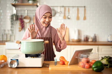 Happy Muslim woman use digital tablet for live stream about cooking in modern Kitchen