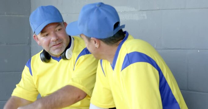 Two baseball teammates entering dugout and sitting on bench, examining baseball grip
