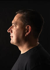 Obraz premium Side profile of man against dark background. Minimalist studio portrait with a serious, moody tone, strong visual focus on facial features.