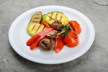 Grilled vegetables with mushrooms in a white plate on a gray background