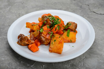 stewed potatoes with meat in a white plate on a gray background