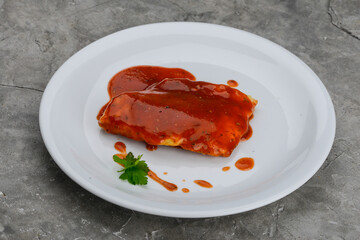 fish fillet in tomato sauce in a white plate on a gray background