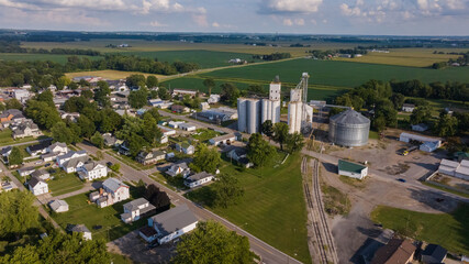 Aerial view of a rural town where silver grain silos pierce the skyline amidst a verdant landscape of fields and homes, West Liberty, Ohio, United States.