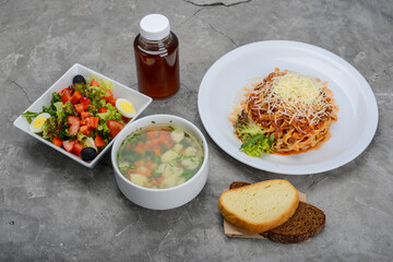 set of pasta with meat and salad on a gray background with bread and a drink
