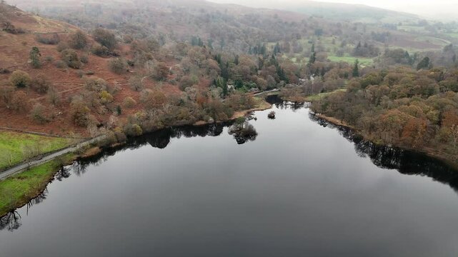 Rydal Water, Aerial view of a serene lake surrounded by trees and hills on an overcast day, road and car visible.