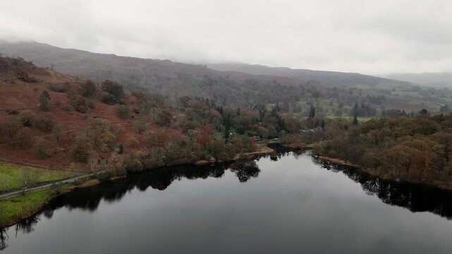Rydal Water, A serene landscape featuring a tranquil lake surrounded by hills and trees under an overcast sky. The water reflects the surrounding scenery.
