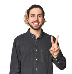 Fototapeta premium Young Caucasian man in studio setting showing victory sign and smiling broadly.