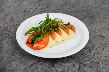 Tomato, cheese salad with pesto sauce and arugula in a white plate