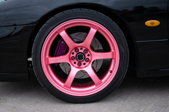 Detail of the front wheel on a JDM street racing and drift sports car, featuring a pink Gram Lights wheel and a modified black brake system