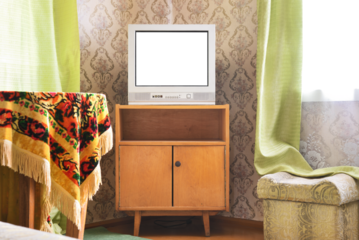 An old TV with a white screen on the bedside table against the background of wallpaper.