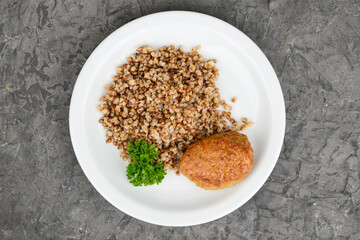 Buckwheat porridge with cutlet in a white plate on a gray background