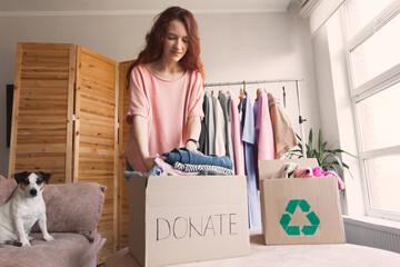 Smiling young woman putting clothing into donation box